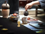 Person pouring tea from a teapot into a cup on a tea table with various tea-making items.