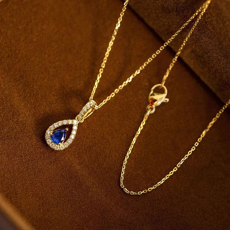 Gold necklace with a blue teardrop pendant on a brown textured surface