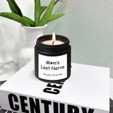 Candle in a black container labeled 'Mom's Last Nerve' on a book with a plant in the background