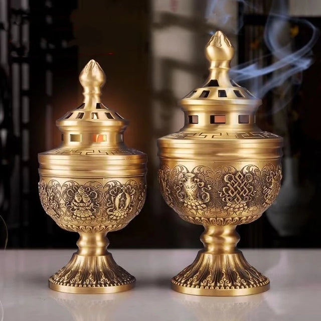 Two ornate gold incense burners with intricate designs on a reflective surface.