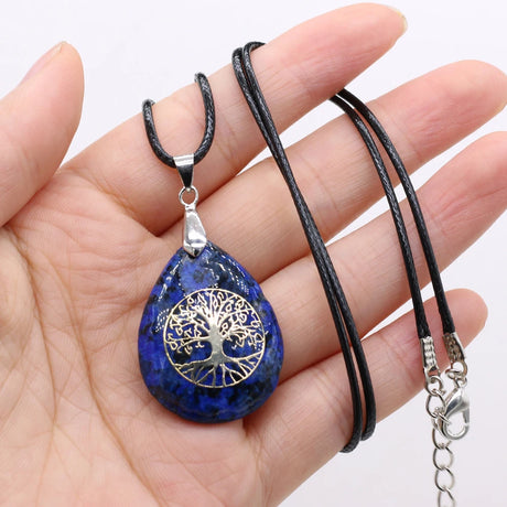 Blue stone pendant with tree of life design on a black cord held in a hand against a white background