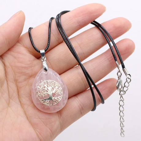 Rose quartz pendant with tree of life design on a black cord held in a hand against a white background