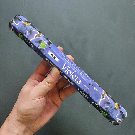 Hand holding a blue and purple product packaging with 'Violeta' branding against a dark background