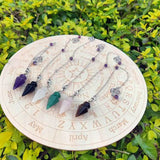 Crystal pendulums on a wooden wheel with astrological symbols against a green leafy background