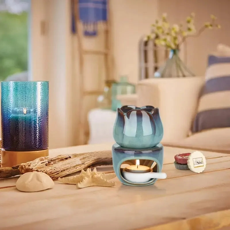 Blue ceramic wax warmer with a lit candle on a wooden surface in a cozy living room.