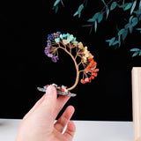 Colorful crystal hair clip held by a hand against a black background with green leaves.
