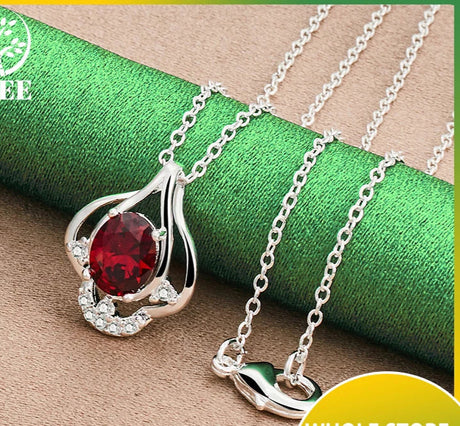 Silver necklace with a red gemstone pendant on a green and brown fabric background, featuring a Tree brand logo.