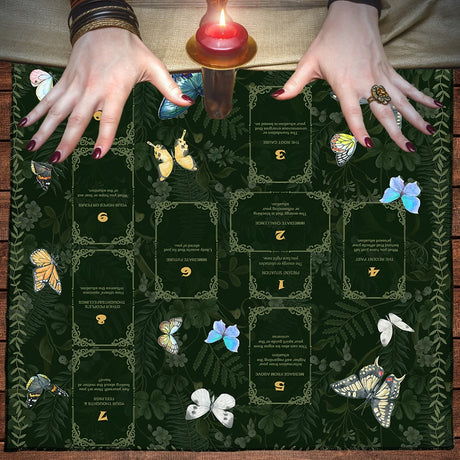 Hands with tarot cards and candles on a dark green cloth with butterfly designs.