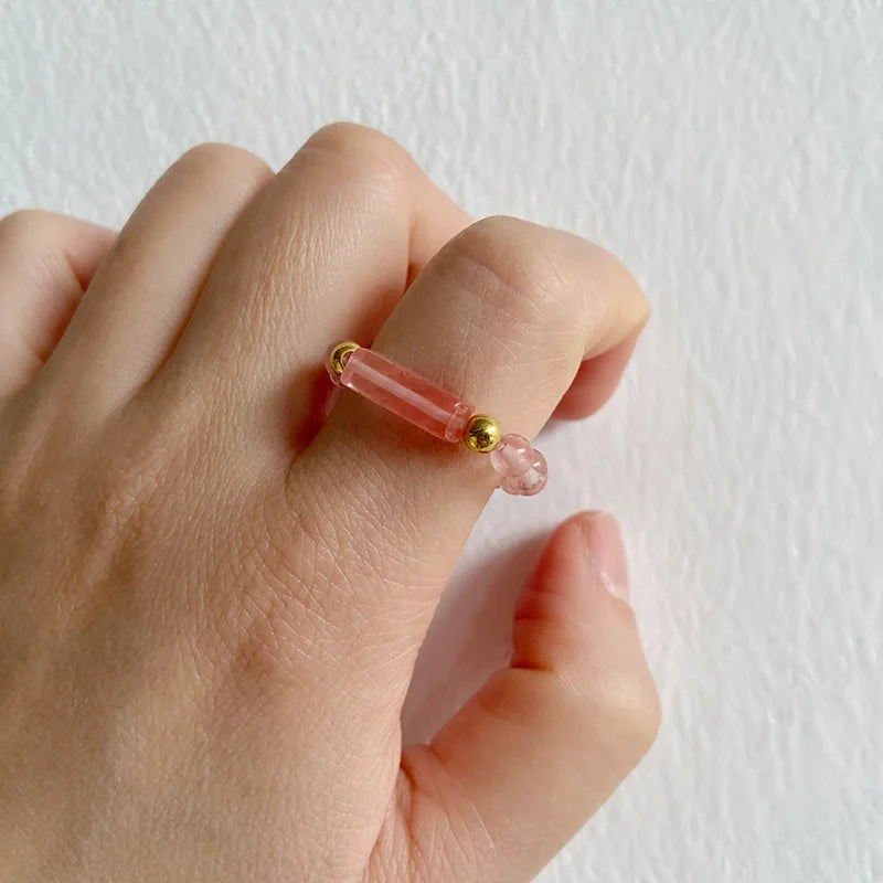 Hand wearing a pink ring with gold accents on a white background