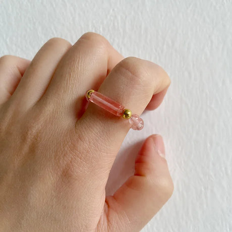 Hand wearing a pink ring with gold accents on a white background