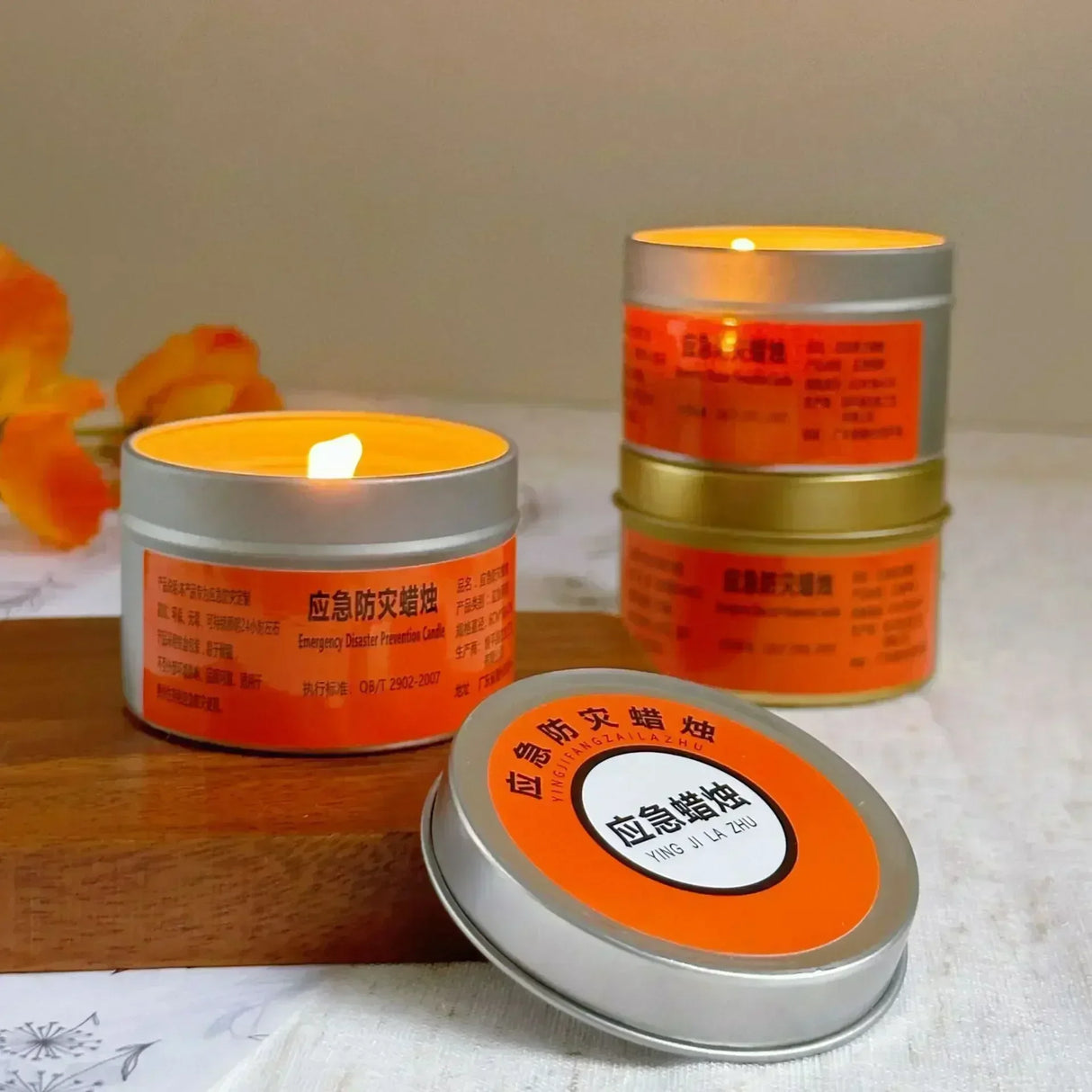 Two lit candles in metal tins with orange labels on a wooden surface.