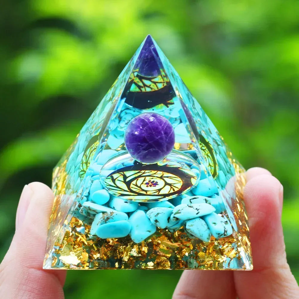 Pyramid-shaped crystal object with a purple ball and turquoise stones held by a hand against a green blurred background
