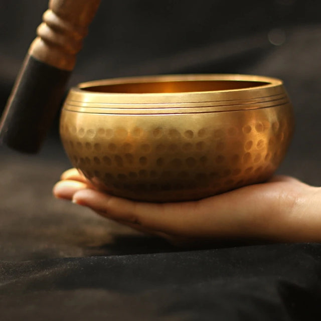 Gold singing bowl held by a hand with a dark background