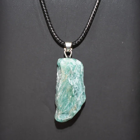 Turquoise stone pendant on a black cord against a dark background
