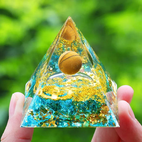 Pyramid-shaped crystal with a gold ball inside, held against a green blurred background