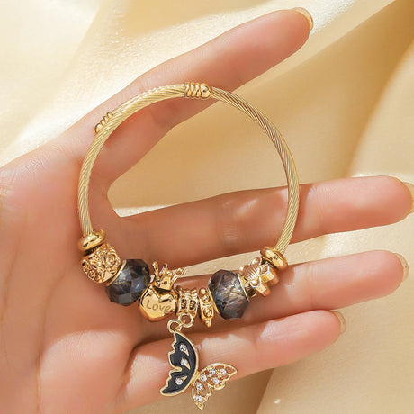 Gold bracelet with charms held by a hand on a beige background