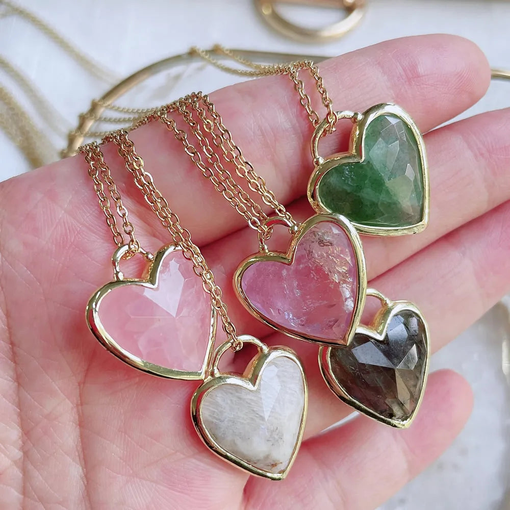 Gold heart-shaped pendants with colorful stones on a hand