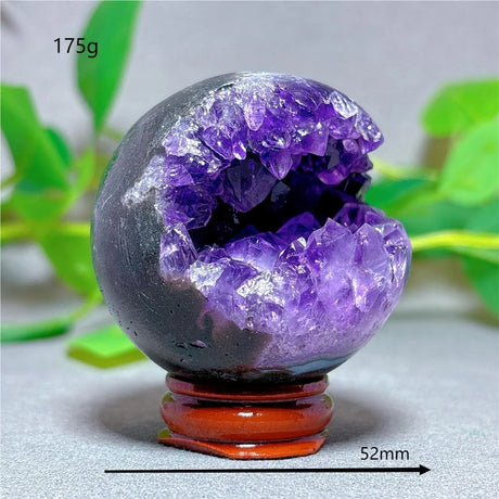 Decorative crystal sphere with purple interior on a stand, surrounded by green leaves.