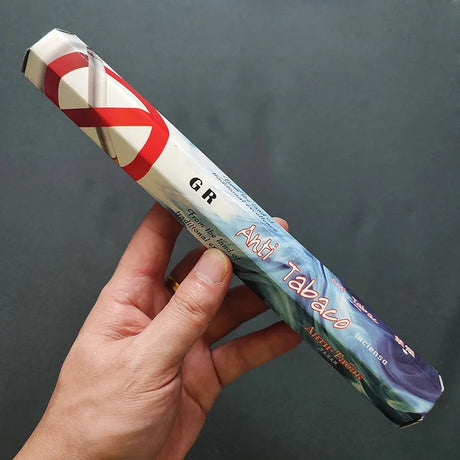 Hand holding a 'Anti Tabaco' product against a dark background