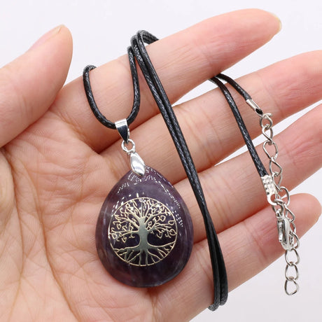 Purple teardrop pendant with tree of life design on a black cord held in hand