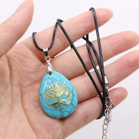 Turquoise pendant with gold tree design held in a hand against a white background