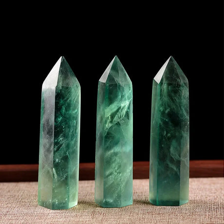 Three green crystal points on a textured surface with a dark background