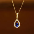 Gold necklace with a blue teardrop pendant on a brown background
