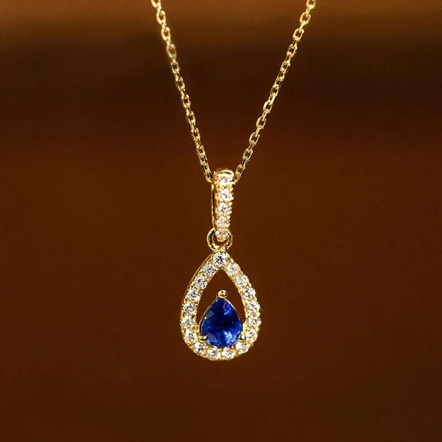 Gold necklace with a blue teardrop pendant on a brown background