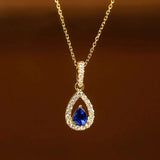 Gold necklace with a blue teardrop pendant on a brown background