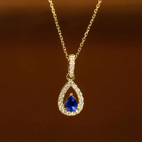 Gold necklace with a blue teardrop pendant on a brown background