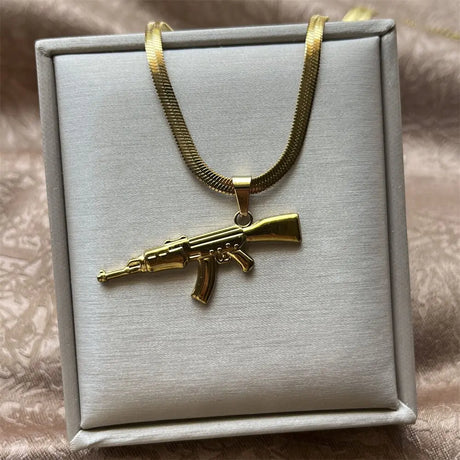 Gold gun-shaped pendant on a gold chain in a gray jewelry box.