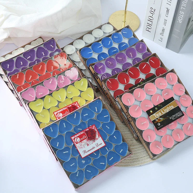 Assorted colorful tea light candles in boxes on a white surface.