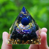 Pyramid-shaped crystal with blue and gold elements held by a hand against a green blurred background
