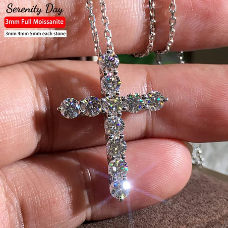Silver cross pendant with clear stones held between fingers, brand 'Serenity Day' visible.