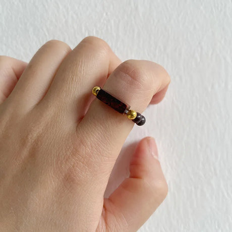 Hand wearing a ring with brown beads on a light background