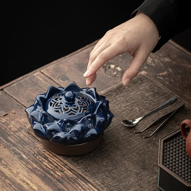 Blue ceramic incense burner on a wooden surface with a hand reaching towards it.
