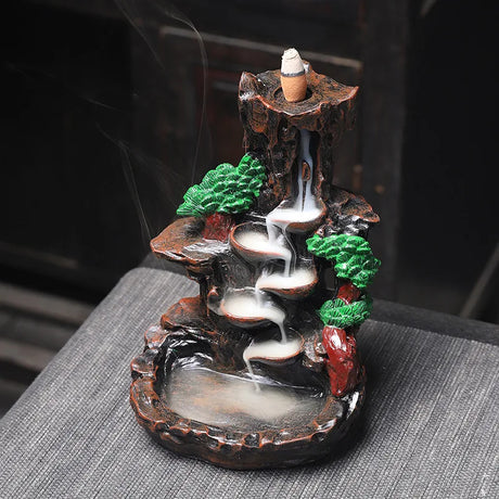 Decorative incense burner with a mountain and tree design on a dark surface.