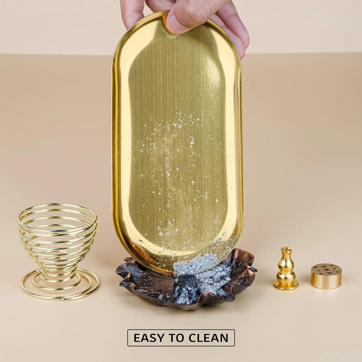 Gold decorative tray with a hand holding it, surrounded by other decorative items on a beige background.