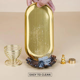 Gold decorative tray with a hand holding it, surrounded by other decorative items on a beige background.