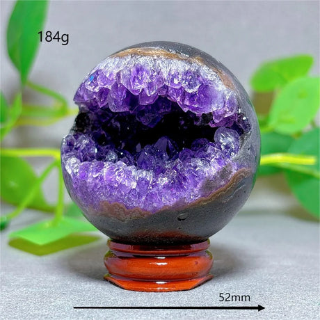 Amethyst geode with a red base on a gray surface with green leaves in the background