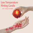 Red candle shaped like a flower held by a hand with red floral designs on another hand against a beige background.