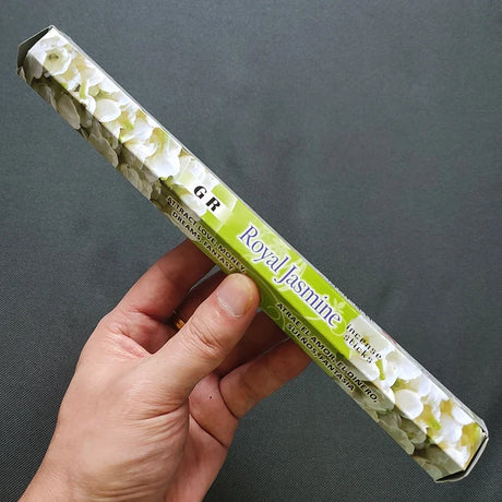 Hand holding a box of Royal Jasmine incense sticks against a dark background