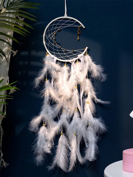 White dreamcatcher with feathers against a dark blue wall