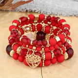 Stack of red beaded bracelets with gold accents and a heart charm on a textured surface.