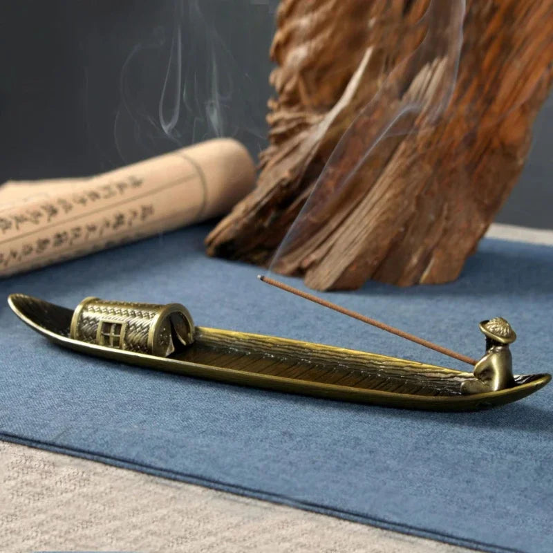 Brass incense burner with incense stick on a blue surface, with wooden elements in the background.