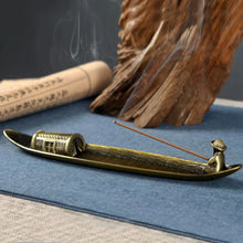 Brass incense burner with incense stick on a blue surface, with wooden elements in the background.