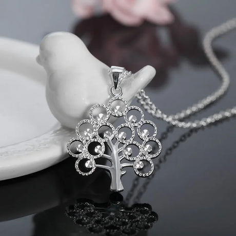 Silver tree-shaped pendant necklace on a dark surface with a blurred background