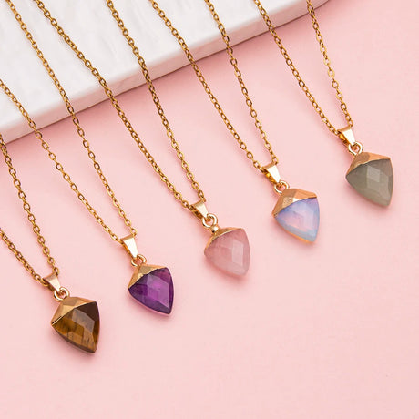 Gold necklaces with various colored gemstones on a pink background
