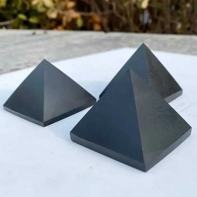 Three black pyramids on a white surface with a blurred natural background