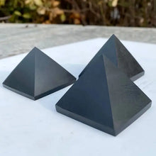 Three black pyramids on a white surface with a blurred natural background